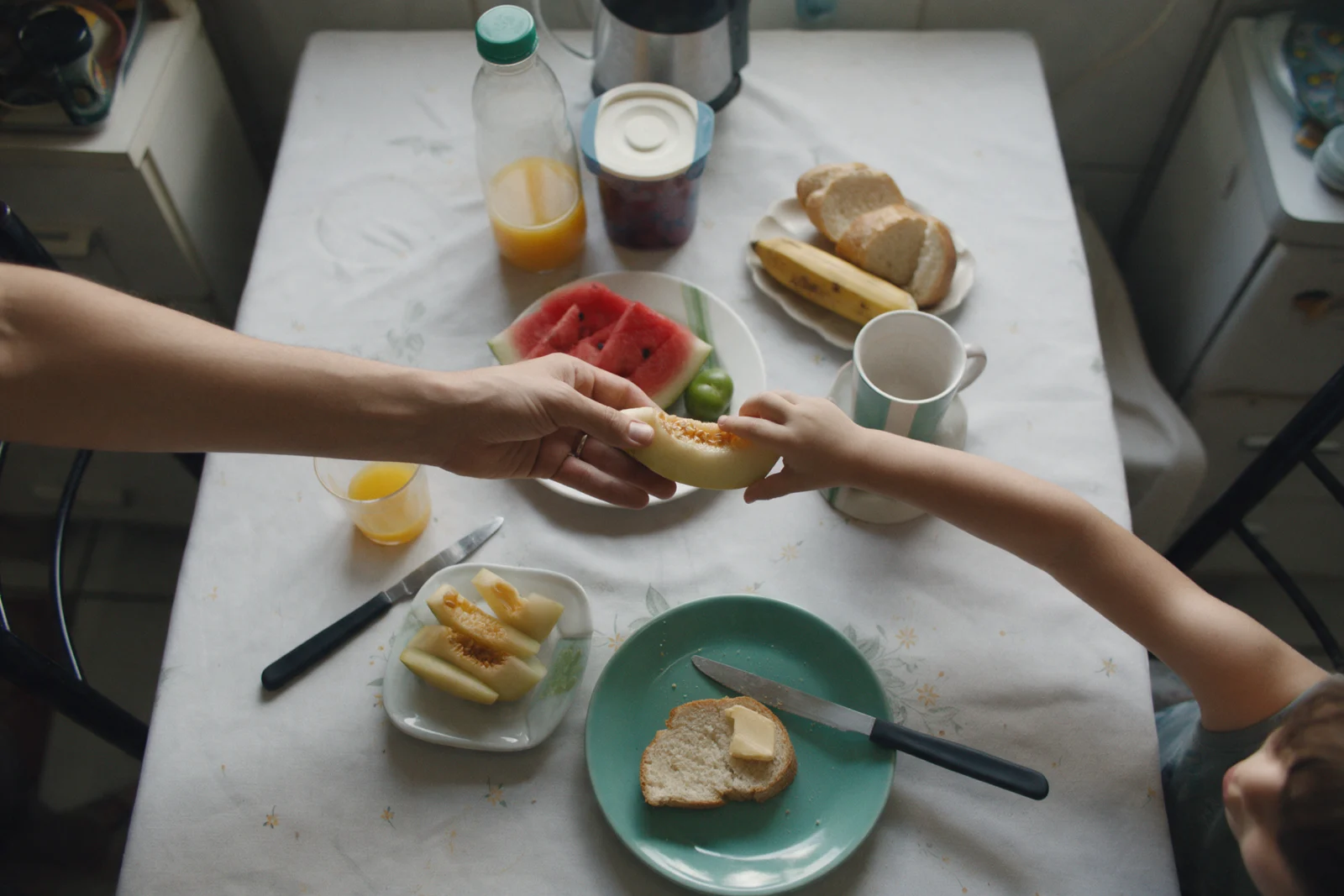 Mãos de um adulto e de uma criança dividindo frutas na mesa do café