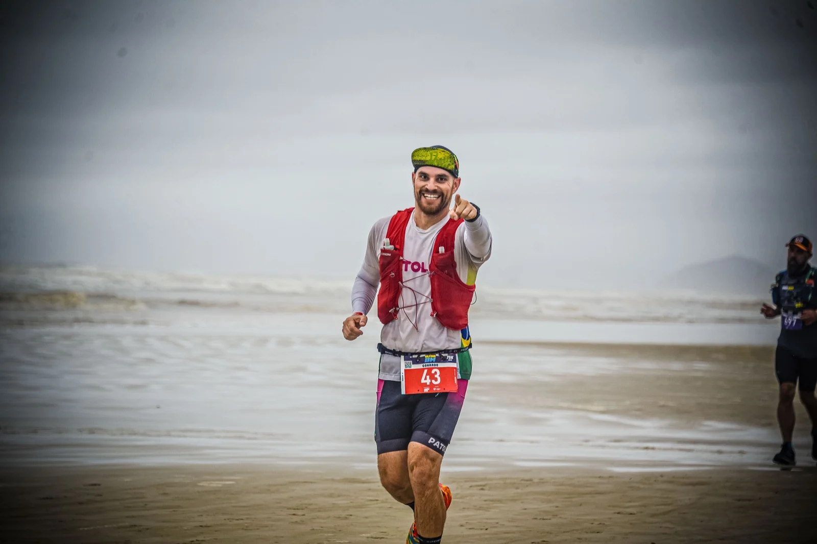 Patoloko correndo na praia durante a BM 75K de 2023 e apontando para a câmera